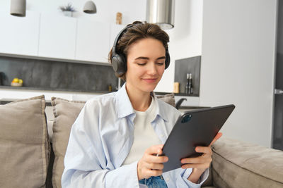 Young woman using digital tablet while sitting on sofa at home