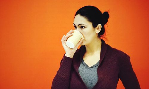 Woman holding disposable cup against orange background