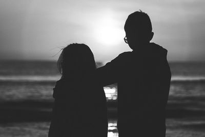 Rear view of silhouette friends standing on shore at beach