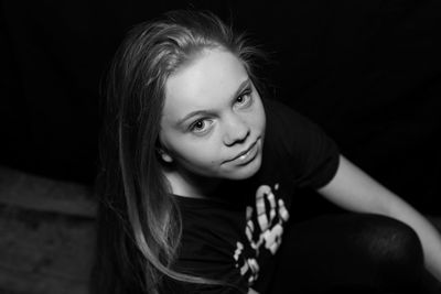 Close-up portrait of smiling young woman against black background