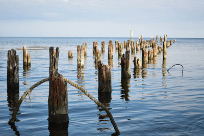 Wooden posts in sea against sky