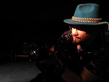 Close-up of man wearing hat while standing against black background