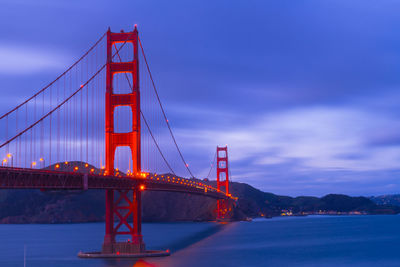 Illuminated golden gate bridge over bay against cloudy sky during sunset
