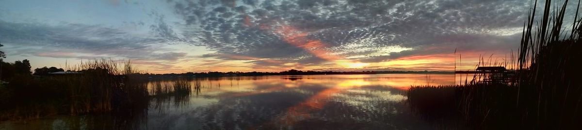 Scenic view of lake against cloudy sky at sunset