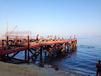 People standing on pier at beach against clear sky