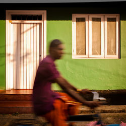 Indian man riding a bicycle along a street past a town house in cochin