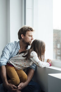 Mature man and girl looking through window at home