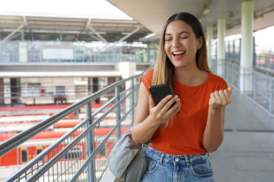 Excited brazilian girl clenches her fist in victory holding smartphone in sao paulo, brazil