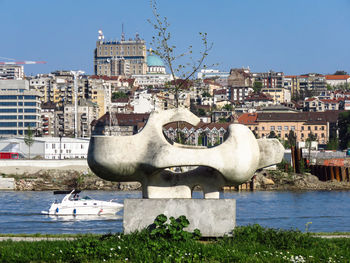 Statue by river against buildings in city