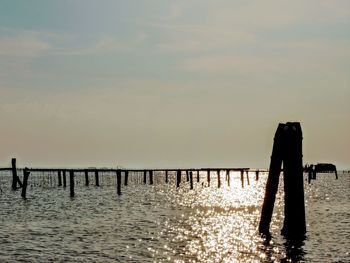 Silhouette man standing on wooden post in sea against sky