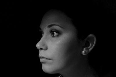 Close-up of serious woman looking away against black background