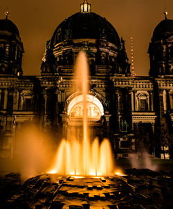 Illuminated fountain against buildings at night