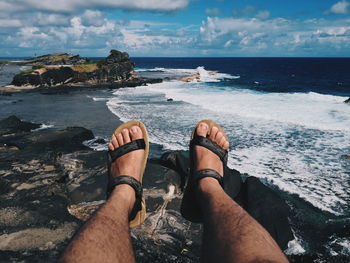 Low section of man sitting on cliff against sea