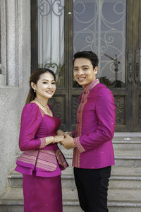 Happy young woman standing against pink building