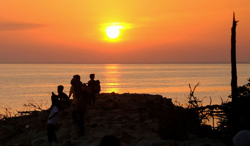 Silhouette people on beach against sky during sunset