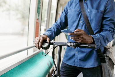 Midsection of man using mobile phone while standing on bus