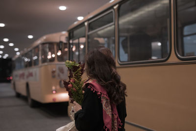 Woman holding bouquet while standing against buses on road at night
