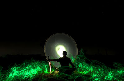 Silhouette man sitting at illuminated lamp at night