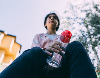 Low angle view of man holding drink sitting outdoors
