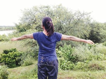 Full length of young woman standing by tree against sky