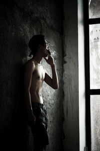 Side view of shirtless young man standing against wall in building