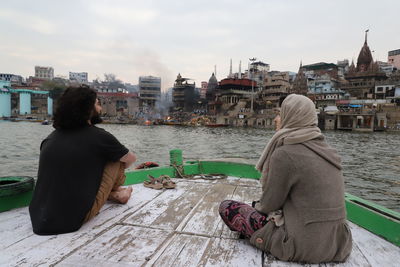 Woman sitting by river in city against sky