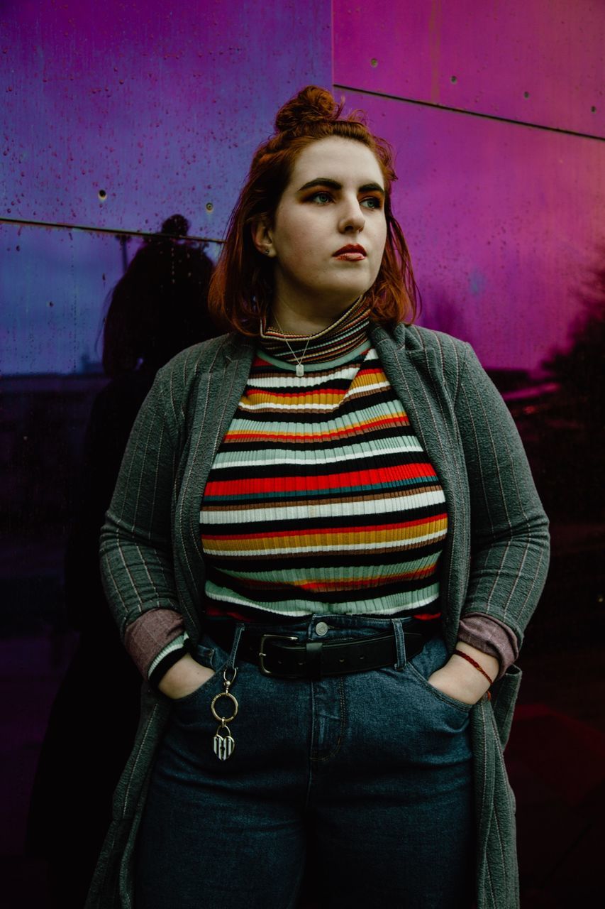 PORTRAIT OF BEAUTIFUL YOUNG WOMAN STANDING AGAINST RED WALL