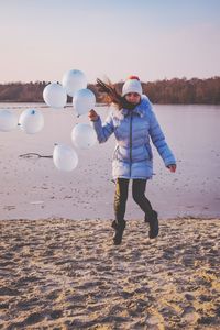 Full length of woman jumping by lake against sky