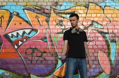 Full length of man standing against graffiti wall