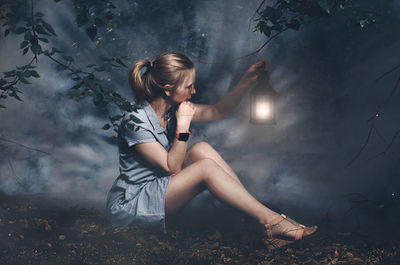 Woman holding illuminated lantern while sitting on land at night