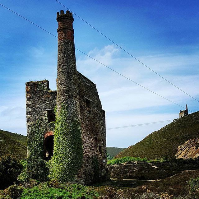 architecture, sky, built structure, building exterior, low angle view, cloud - sky, field, landscape, cloud, blue, power line, hill, old, nature, tower, no people, fuel and power generation, outdoors, house, day