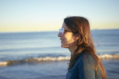Smiling young woman wearing sunglasses at beach against sky during sunset