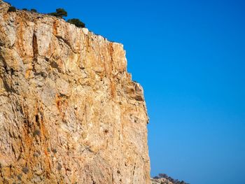 Low angle view of rocky mountain against clear blue sky