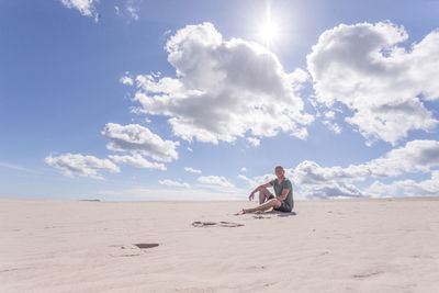 Man sitting on sand dune in desert against sky