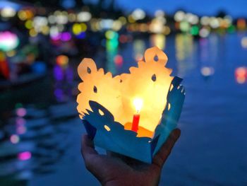 Close-up of hand holding lit candle against blurred background