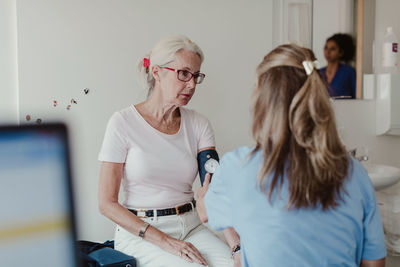 Female doctor checking blood pressure of senior woman in clinic