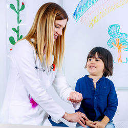 Smiling female doctor checking girl wrist in hospital