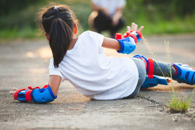 Rear view of girl falling while doing inline skating on road