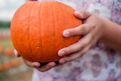 Cropped image of hand holding pumpkin against orange background