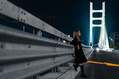 Side view of young woman walking on illuminated city street at night