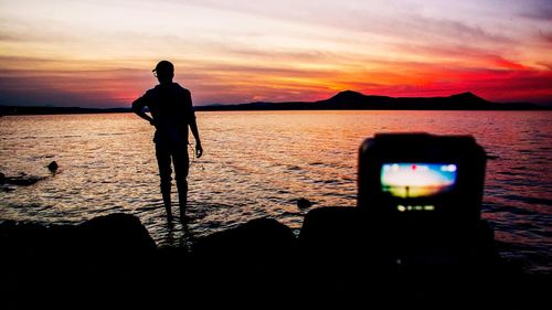 Silhouette man photographing sea against sky during sunset