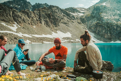 People sitting by lake against mountains