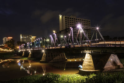 Illuminated bridge over river in city against sky at night