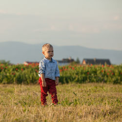 Cute boy standing on field against sky