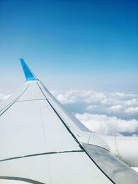 Cropped airplane flying over clouds against blue sky