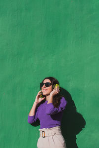 Young woman wearing sunglasses standing against green wall