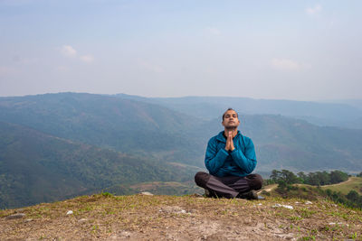 Man meditating at hill top with misty mountain rage background from flat angle