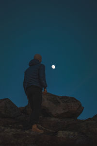 Rear view of man standing on rock against clear blue sky