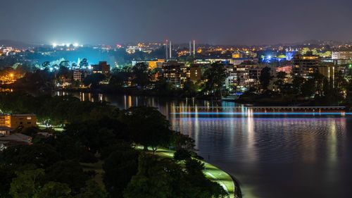 Illuminated cityscape by river against sky at night