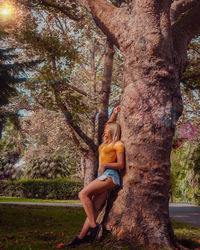 Side view of woman sitting on tree trunk in forest